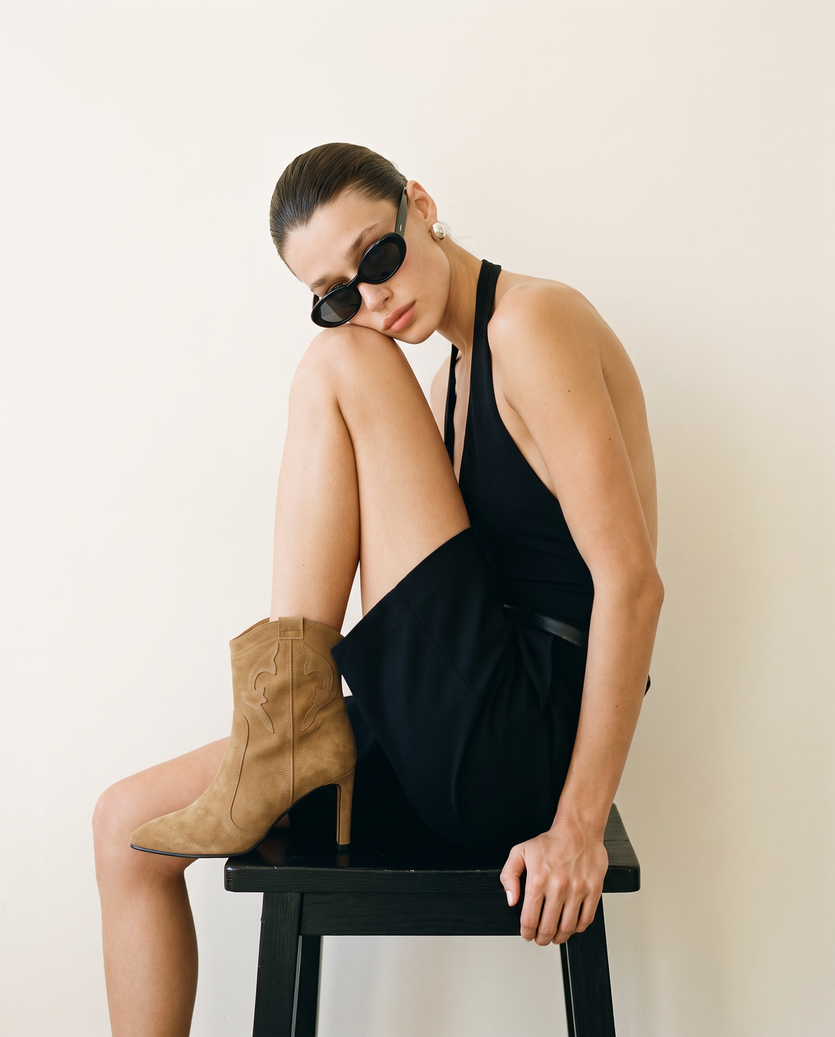 Model wearing ASADLIE Blair camel suede ankle boots with pointed toe and slim heel, seated on a black stool