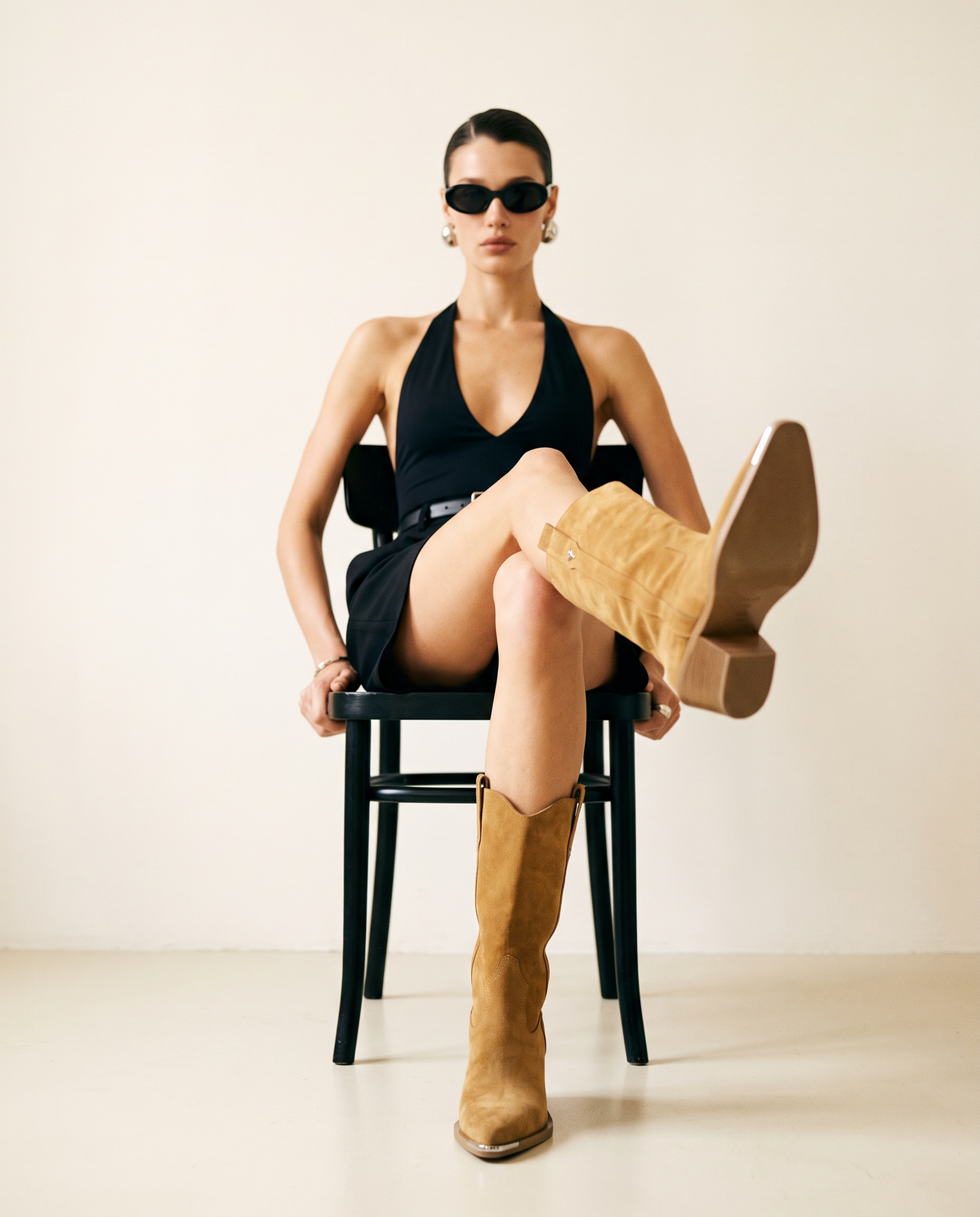 ASADLIE Nova camel suede cowboy boots on a seated model with crossed legs, showing the block heel, sole and metal toe